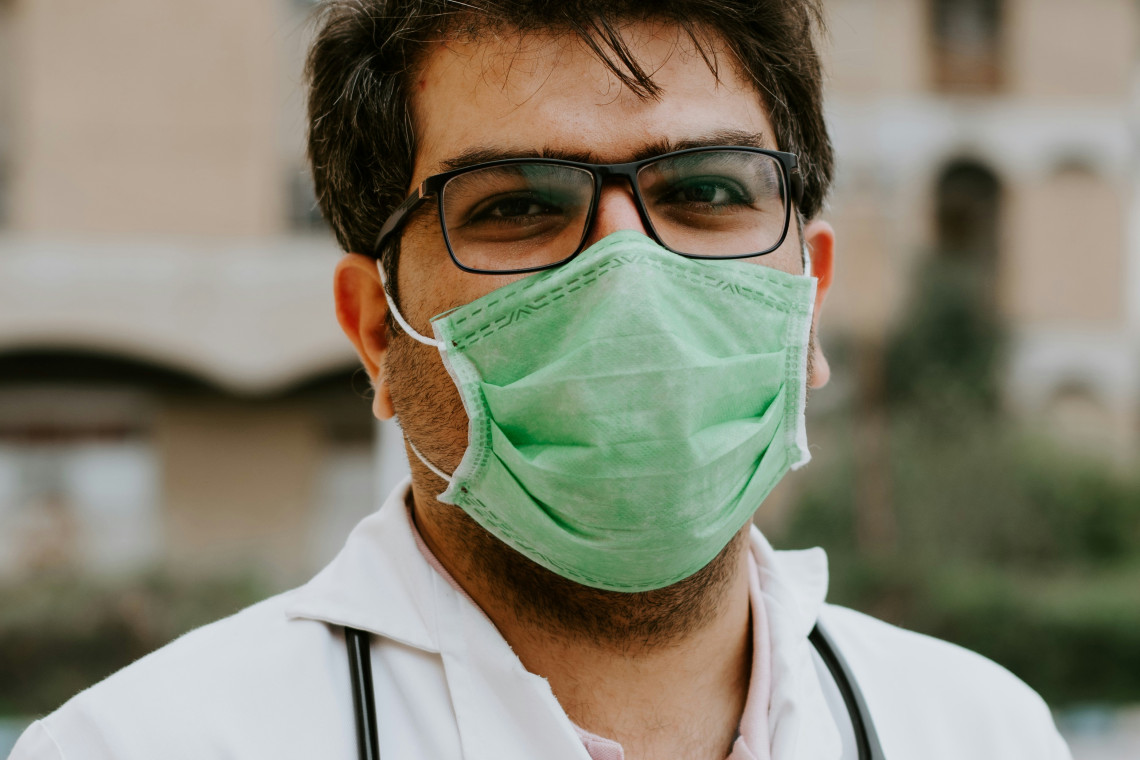 man in white scrubs wearing green mask