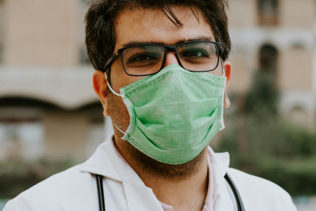 man in white scrubs wearing green mask