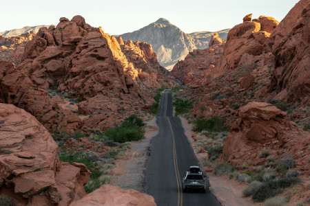 solo black car driving on 2-lane highway through desert mountain terrain