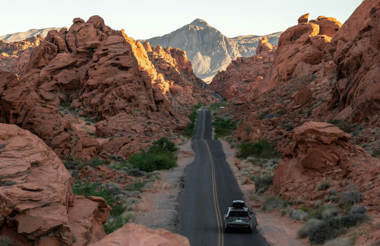 solo black car driving on 2-lane highway through desert mountain terrain