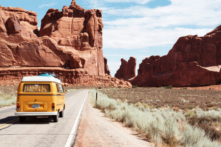 Yellow Volkswagen Westfalia driving through red rock canyon desert road