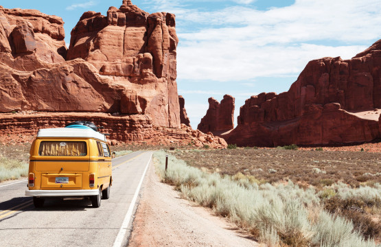 Yellow Volkswagen Westfalia driving through red rock canyon desert road